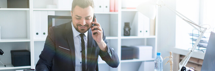 A man is sitting at the desk at the office, talking on the phone and taking a marker in his hand.