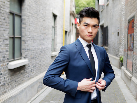 Portrait of a handsome businessman in suit posing outdoor, close up upper body view. Attractive male hipster Chinese model.