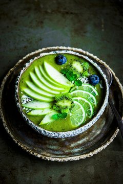 Green smoothie bowl with spinach, banana, apple, coconut water, limes, kiwi flowers and blueberries