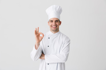 Handsome young man chef indoors isolated over white wall background.