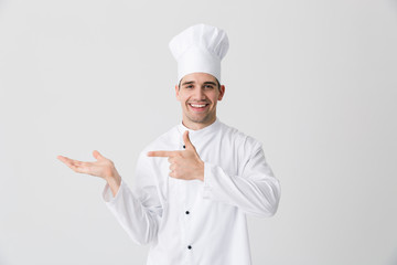 Excited young man chef indoors isolated over white wall background pointing.