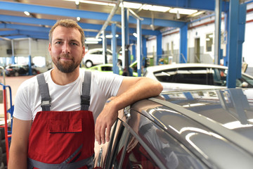 portrait of a friendly car mechanic in the workshop as a closeup - profession and training //...