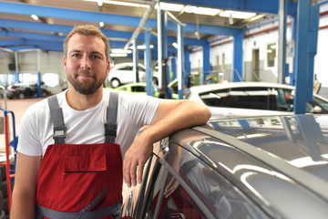 portrait of a friendly car mechanic in the workshop as a closeup - profession and training // lächelnder Automechaniker in einer Werkstatt zur Reparatur von Fahrzeugen