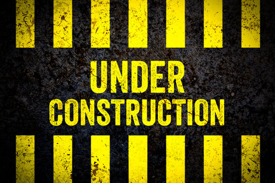 Under construction warning sign with yellow and black stripes painted over cracked concrete wall weathered texture background. Concept for do not enter the area, caution, danger, construction site.