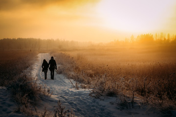 silhouette of a couple walking in the snowy road on sunset