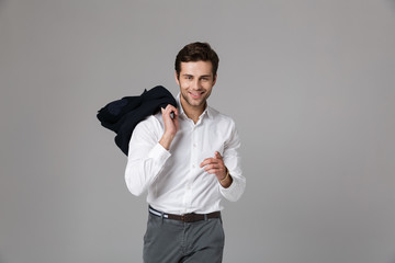 Image of brunette businessman 30s smiling and holding jacket over his shoulder, isolated over gray...