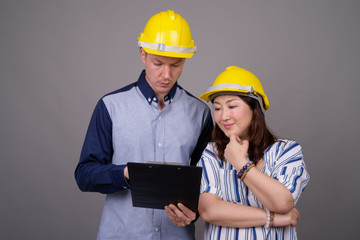 Businessman and mature Asian businesswoman wearing hardhat