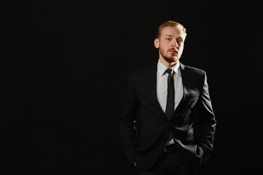 Portrait of sexy handsome confident man with beard standing on black background in suit. Copy space. Leadership concept.