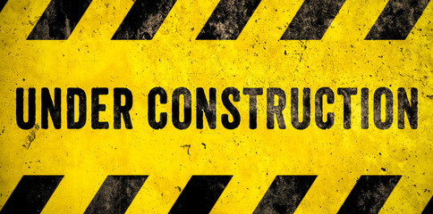 Under construction warning sign text with yellow black stripes painted over concrete wall cement...