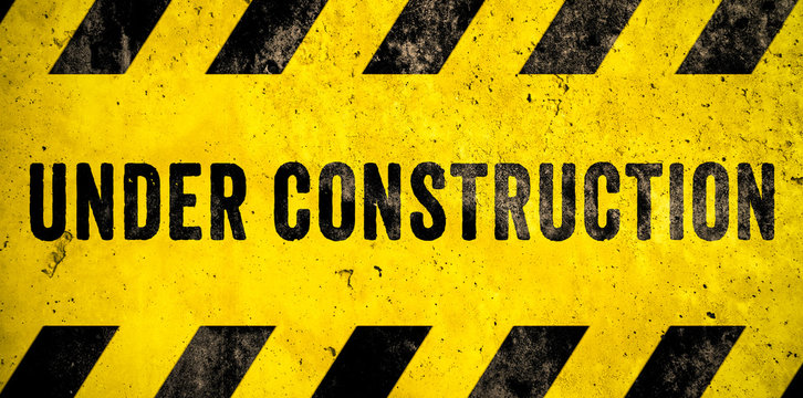 Under construction warning sign text with yellow black stripes painted over concrete wall cement facade as texture background banner. Concept do not enter area, caution, danger, construction site.