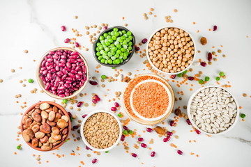 Various assortment of legumes - beans, soy beans, chickpeas, lentils, green peas. Healthy eating concept. Vegetable proteins. White marble background copy space top view - obrazy, fototapety, plakaty