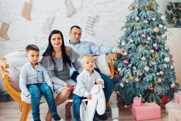 Happy Young Family With Two Children is waiting Christmas t and Smiling at Camera Near Christmas tree. New Year Celebration. Decorations.  Xmas event