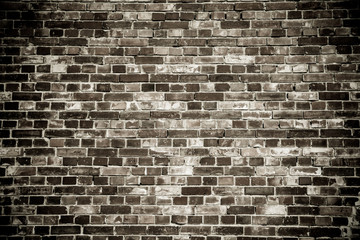 Old and weathered grungy black dark gray concrete block brick wall surface texture background with vignetting.