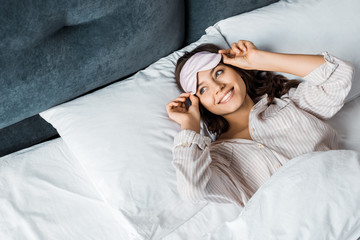 smiling girl in sleeping mask waking up in bed in the morning - obrazy, fototapety, plakaty