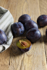 Fresh prune plums, one cut, on wooden surface