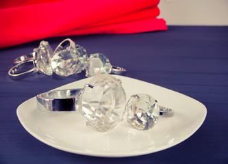 Two diamond rings on the white plate. In the background a bunch of rings.