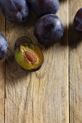Fresh prune plums, one cut, on wooden surface