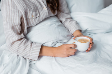 cropped view of woman with cup of cappuccino in bed