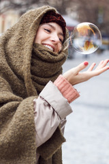 Portrait of a beautiful woman as she tries to catch bubbles in a cold winter in the historic district. She's wearing a winter jacket, headband and her head is wrapped in a green scarf.