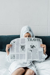 confused girl hiding behind travel newspaper while resting on bed in the morning