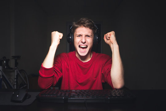 Joyful young man with headphones at home playing a computer game. Gamer happy for the win. Happy young man in headphone uses a computer. Gamer plays games on the computer
