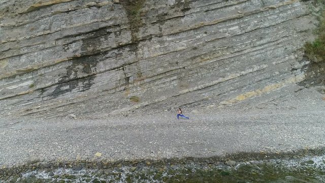 Woman is doing yoga and stretcing exercises on rock and sea background. Aerial beautiful footage side view.
