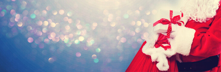 Santa holding a present box from a red sack on a shiny light background