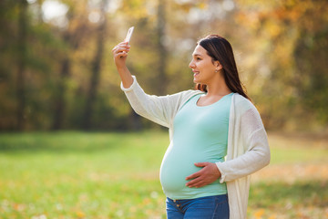 Pregnant woman relaxing in park. She is taking selfie. 