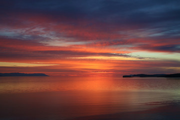 Bay at sunset. Bright sunrise landscape in sea. Flaming colors of early morning. Dawn silence on lake.