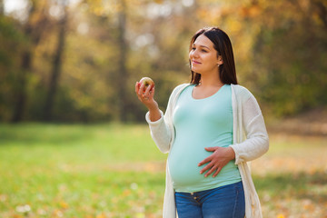 Pregnant woman relaxing in park. She is eating apple. 