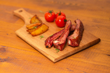 Pork ribs served with tomato and fried potato on wooden table.