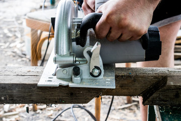 A man works with his hands and a construction tool. Electric saw. Work on wooden boards. To cut the materials. Fine shavings flying in all directions.