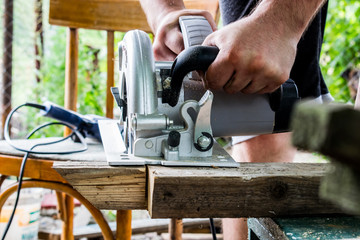 A man works with his hands and a construction tool. Electric saw. Work on wooden boards. To cut the materials. Fine shavings flying in all directions.
