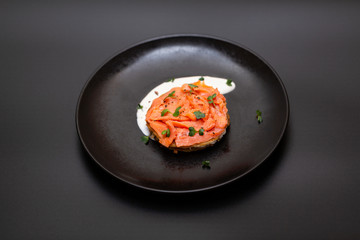 Black plate with smoked salmon on a potato pancake with sauce. Tasty snack