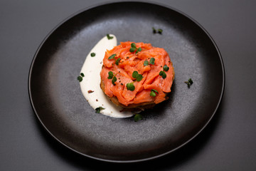 Black plate with smoked salmon on a potato pancake with sauce. Tasty snack