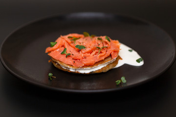 Black plate with smoked salmon on a potato pancake with sauce. Tasty snack