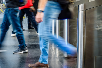 Side view of men passing through stainless steel ticket gates in a public transportation station in Paris, France, with motion blur.