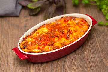 Italian food. Hot tasty freshly baked lasagna served with basil herb on wooden table.