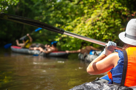Young woman in kayak with oar in wild river. Group friends in canoe