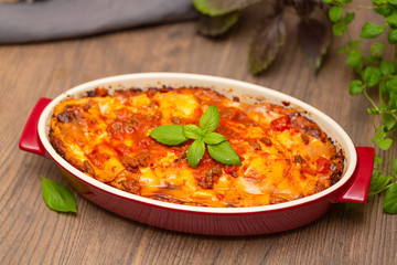 Italian food. Hot tasty freshly baked lasagna served with basil herb on wooden table.