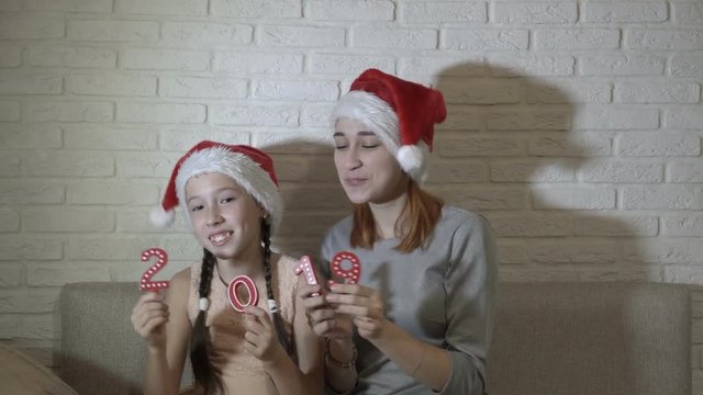 Children in Santa Claus hats holding figures 2019, sitting together on the couch, dancing and smiling. Symbol of new year. 4K. 25 fps.