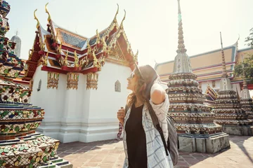 Papier Peint photo Bangkok Jeune belle femme européenne souriante heureuse dans un chapeau et des lunettes dans un temple bouddhiste à Bangkok voyageant en Asie du sud-est