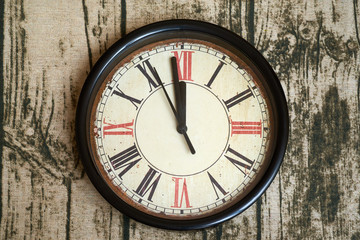 Old style classic clock with roman numbers showing almost twelve o' clock. Time almost gone or came,  on wooden texture background, front view
