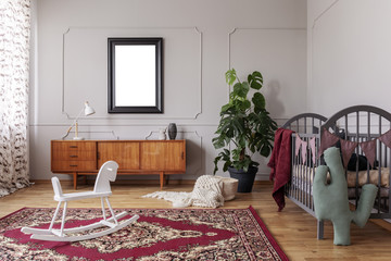 White rocking horse on carpet in grey child's bedroom interior with mockup of poster. Real photo