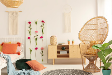 Wicker peacock chair with patterned pillow in cozy bedroom interior with macrame on the wall,...