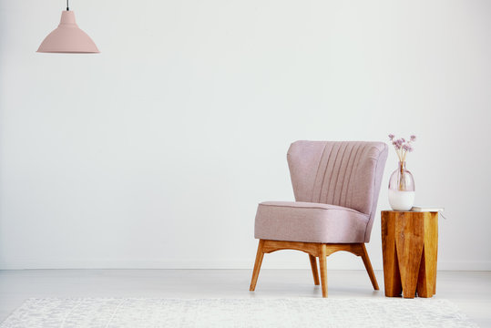 Pink armchair next to wooden table with plant in flat interior with lamp and copy space. Real photo