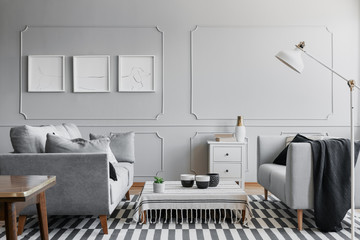 Grey spacious living room with two comfortable sofas and small coffee table covered with striped tablecloth, real photo with mockup on the wall