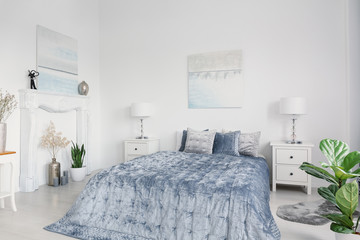 Blue bed with cushions between cabinets with lamps in white bedroom interior with posters. Real...