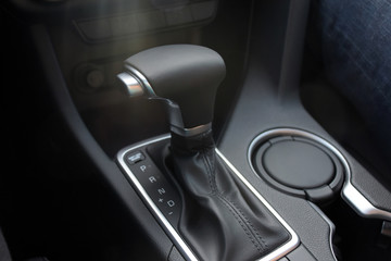 Car interior indoor. Black leather automatic gearbox with chrome button and sun rays, round ashtray 