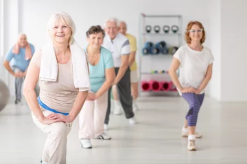 Gardinen Smiling senior woman with towel exercising during fitness classes for elderly people © Photographee.eu